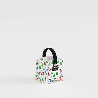 A small structured square gift bag in white with an all-over print of dachshunds in colorful sweaters and green evergreen trees, featuring a black webbing handle and a silver grommet detail on the front.