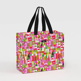 A large structured gift bag with black woven handles featuring a colorful geometric holiday print in pink, red, lime green, and white with festive motifs including trees, deer, ornaments, and candy canes.