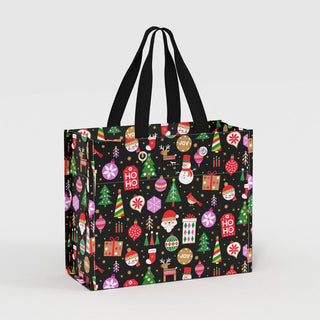 A large structured tote-style gift bag with a black background covered in a colorful holiday icon print including Christmas trees, ornaments, snowmen, Santa, and gift boxes, with black woven carry handles.