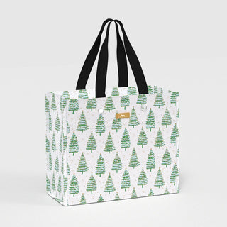 A large structured rectangular gift bag with an all-over green evergreen tree print on a white background with gold accent dots, featuring black woven webbing handles and silver-tone grommets.