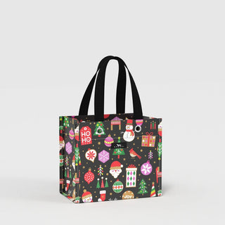 A structured, box-shaped small gift bag with a black background covered in multicolor holiday icons — Santa, snowmen, Christmas trees, ornaments, and gift boxes — featuring a clear vinyl front panel and dual black woven handles with metal grommets.