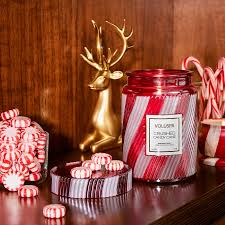 Decorative setup with Voluspa candle, candy canes, and a gold deer statue on a wooden surface.
